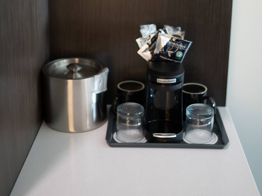 A coffee maker with four cups on a tray, a metal container, and a wooden wall.