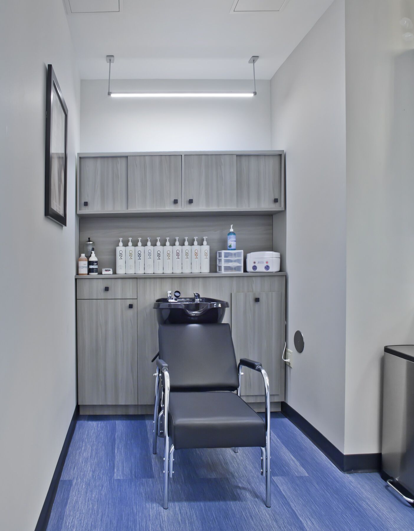 A clinical room with a single reclining chair, a sink, and a cabinet with hygiene products.