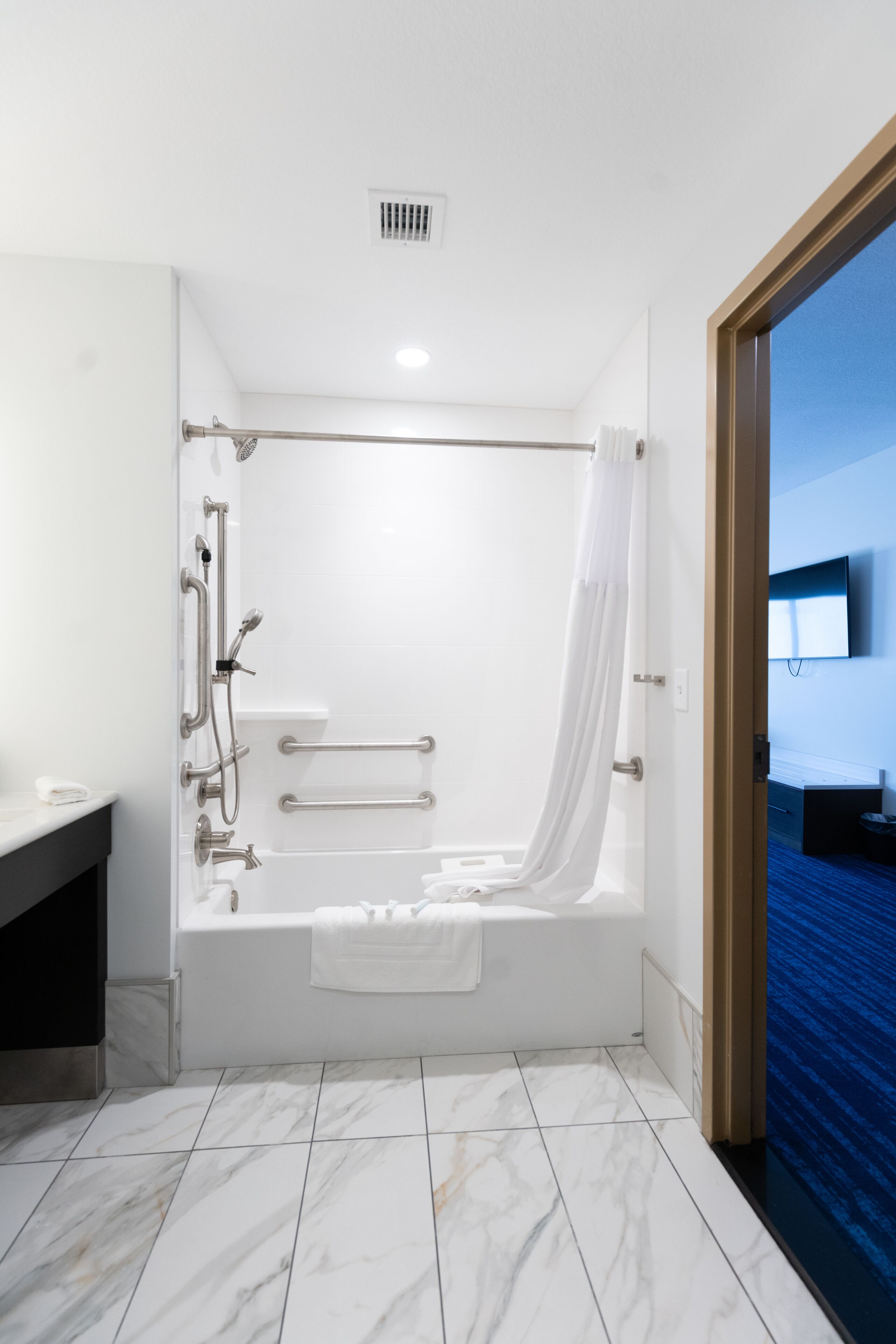 A modern bathroom with a bathtub, shower, and handrails.