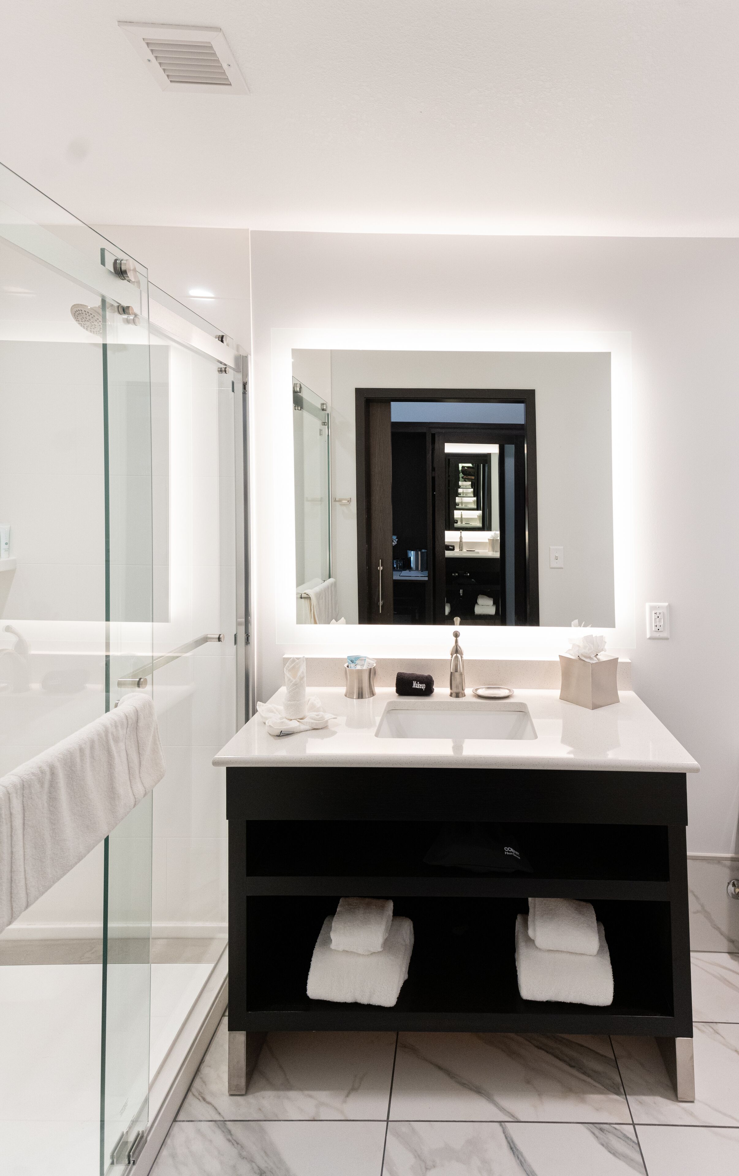 A modern bathroom with a glass shower enclosure, a large mirror, and a dark vanity with a towel rack.