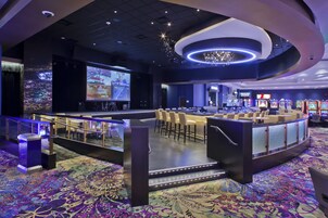 Zona de bar moderna con pantalla grande, asientos y máquinas de juego.