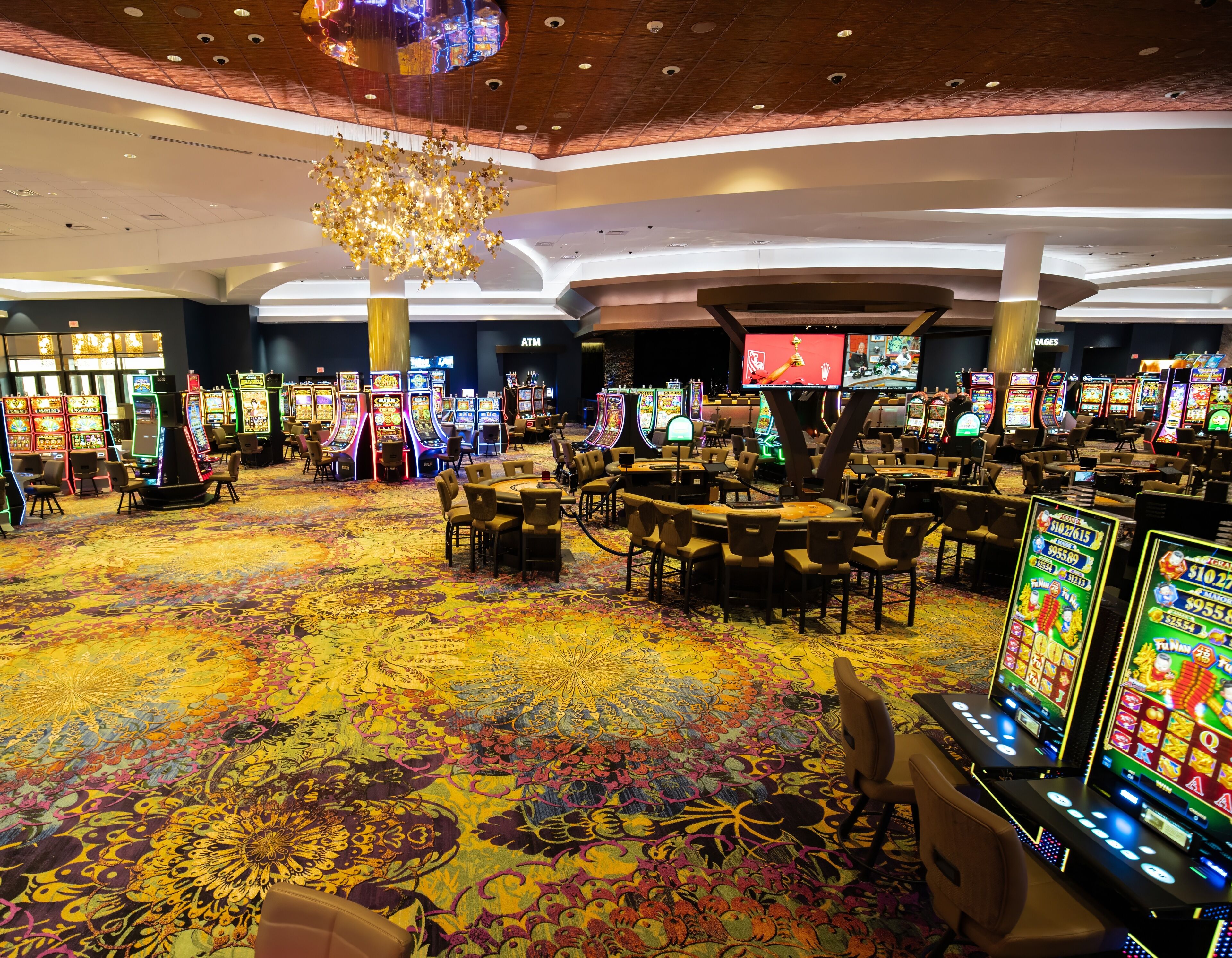 Un casino con numerosas máquinas tragamonedas, mesas para juegos de cartas y una gran lámpara de cristal.