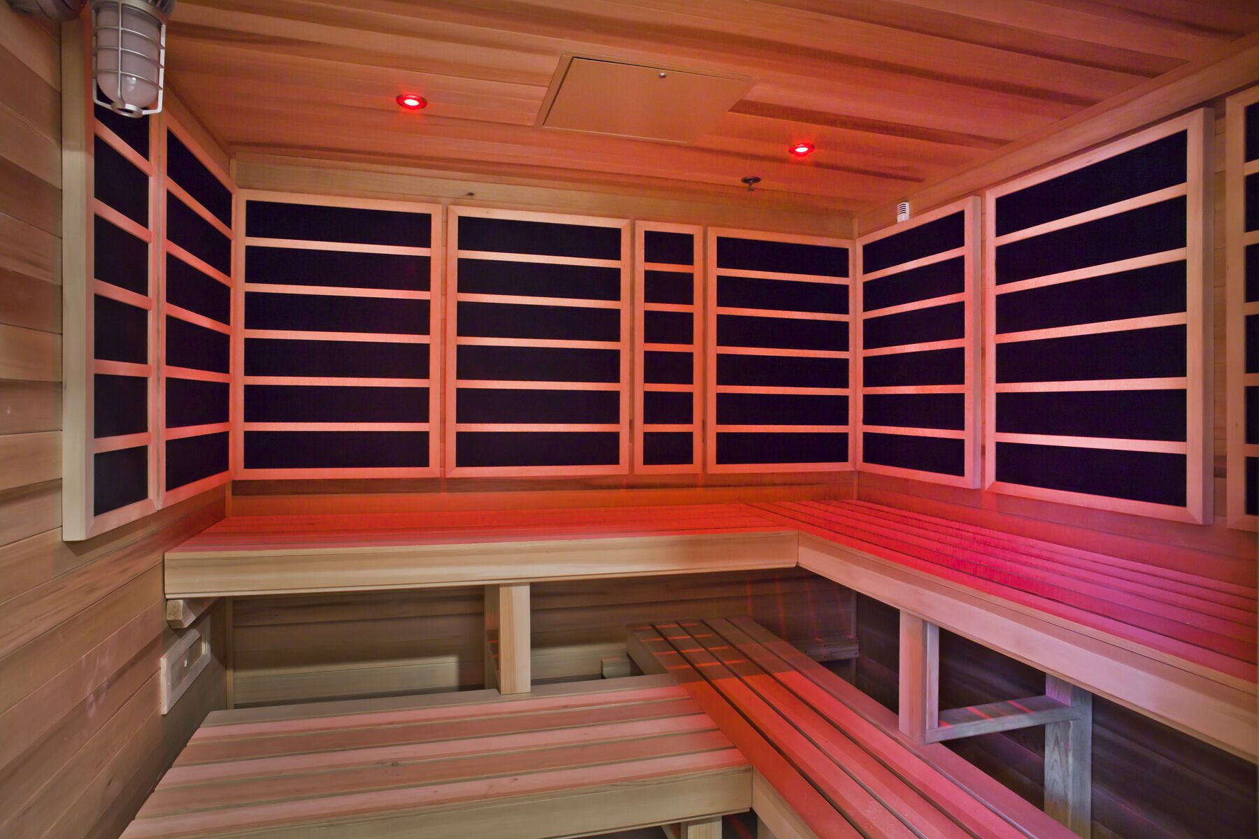 A sauna with wooden benches and walls, featuring a sloped ceiling and red lighting.