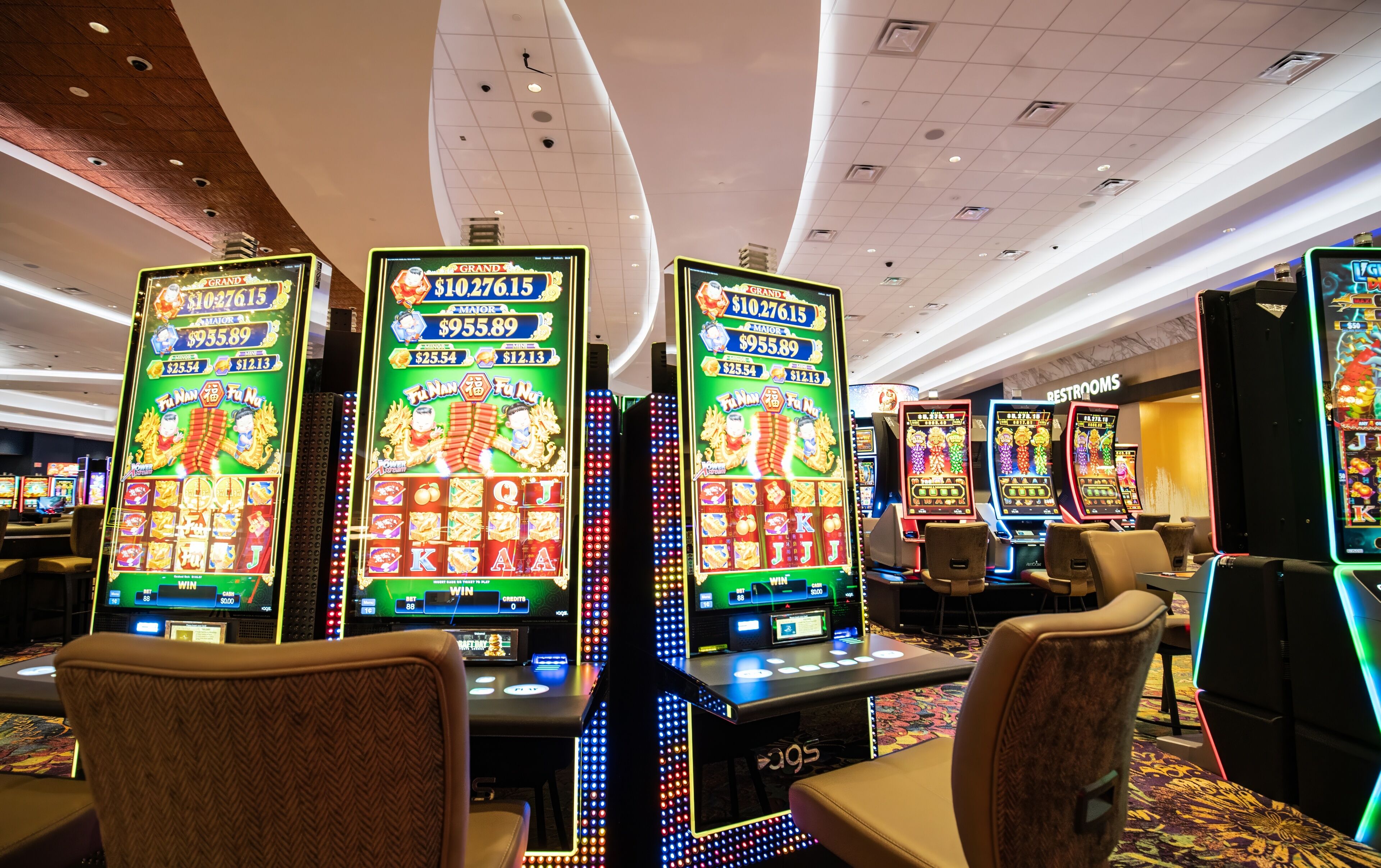 Un casino con varias máquinas tragamonedas, sillas y un letrero que indica el baño.