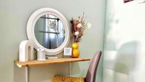 A small, private bathroom with a vanity, a mirror, a toilet, and a shelf with a vase of flowers.