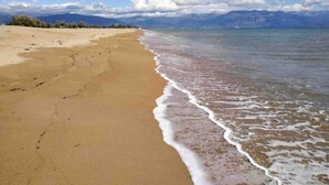 A beach with a clear sky, mountains in the background, and a calm sea.
