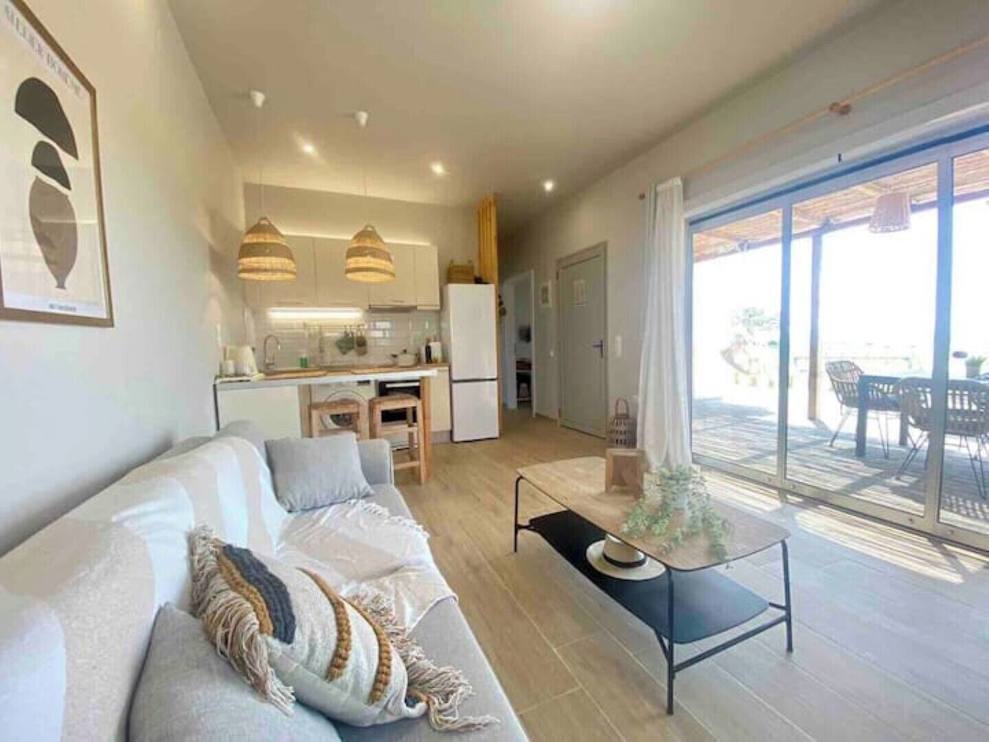 Un salon moderne avec un canapé, une table basse et une vue sur un balcon aménagé avec du mobilier d’extérieur.