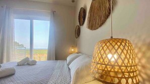A hotel room with a bed, a nightstand, a lamp, and a view of the outdoors.