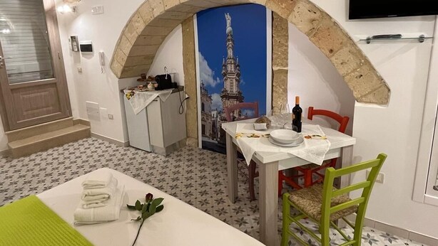 A compact room with a dining area, a bed with neatly folded towels, a green chair, and a TV mounted on the wall. - Studio apartment on padreterno street in nardò to relax, 5 minutes from the beach  (Nardò)