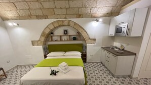 A bedroom with a green bed, a small kitchenette, and a stone archway. - Studio apartment on padreterno street in nardò to relax, 5 minutes from the beach  (Nardò)