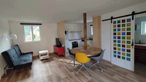 Un espacio habitable compacto con zona de comedor, kitchenette, sofá y televisor sobre un mueble.