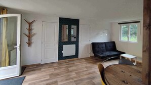 Una habitación amplia con piso de madera, un sofá negro, una mesa de comedor y un ventanal grande.