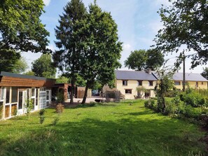 A residential area with two houses, one with a wooden facade and the other with a yellow exterior. There is a grassy yard in front of the houses, and a large tree is visible. - Vacation home for 4–6 people on a large, fenced-in lot (pets welcome!) (La Chapelle du Lou du Lac)