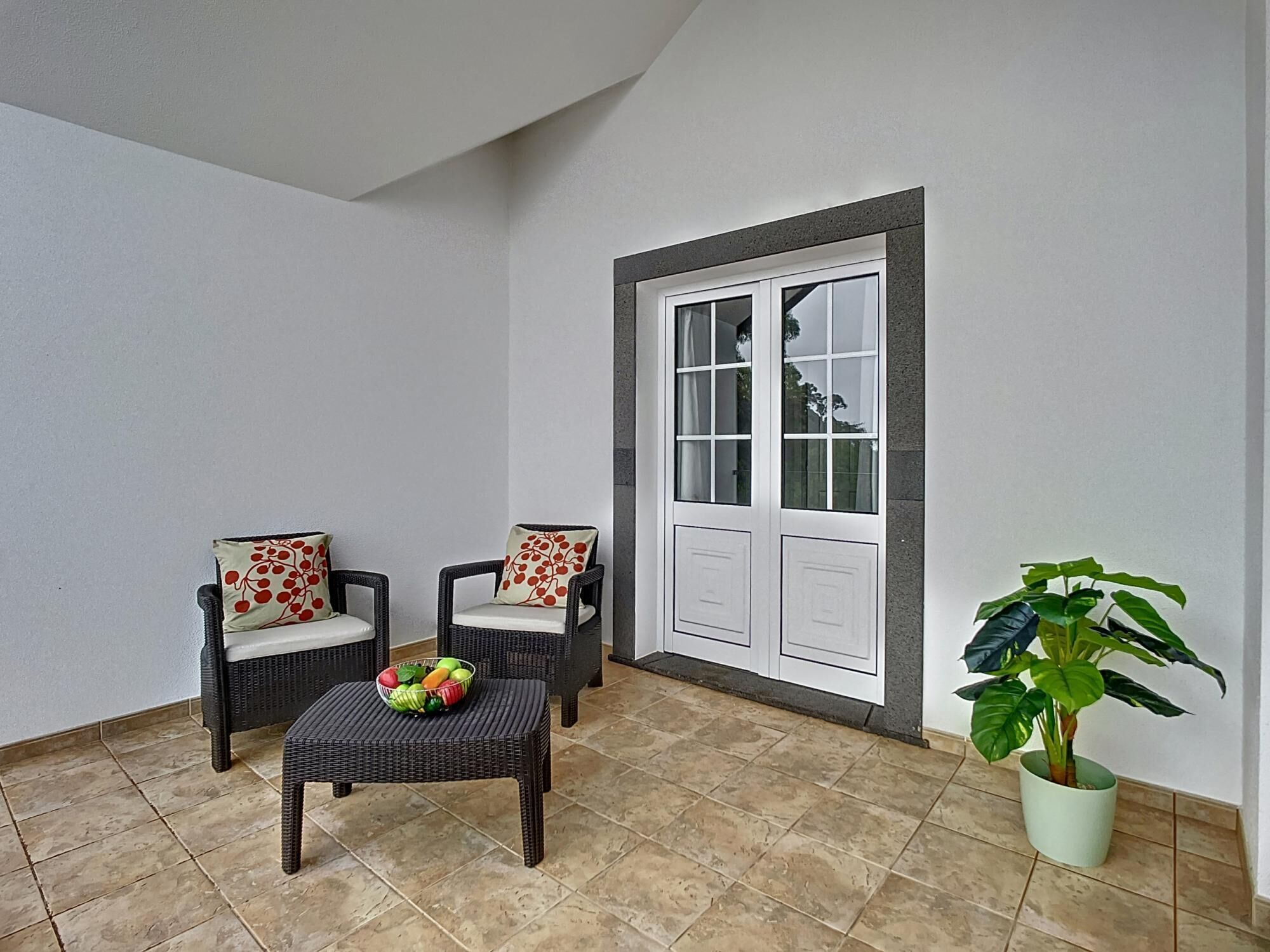 A balcony with wicker chairs, a small table with fruit, and a potted plant.