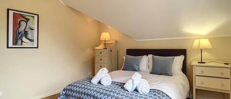 A bedroom with a bed, two bedside tables, a nightstand, a painting, and a wooden floor.