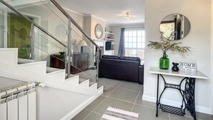 Un interior moderno con una escalera, una sala de estar con sofá, una mesa de comedor y un espejo.