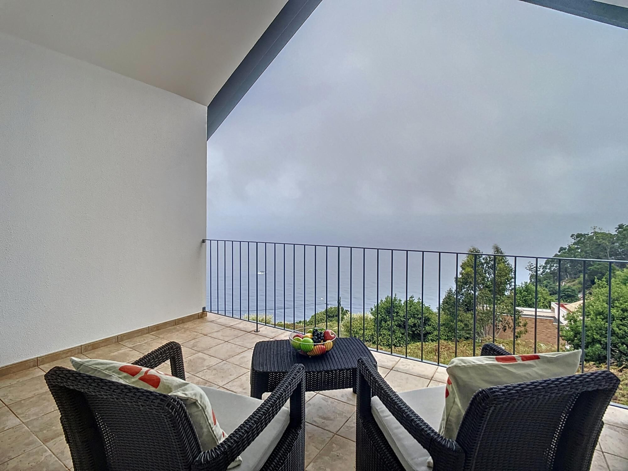 A balcony with wicker furniture and a table, overlooking a body of water and greenery.