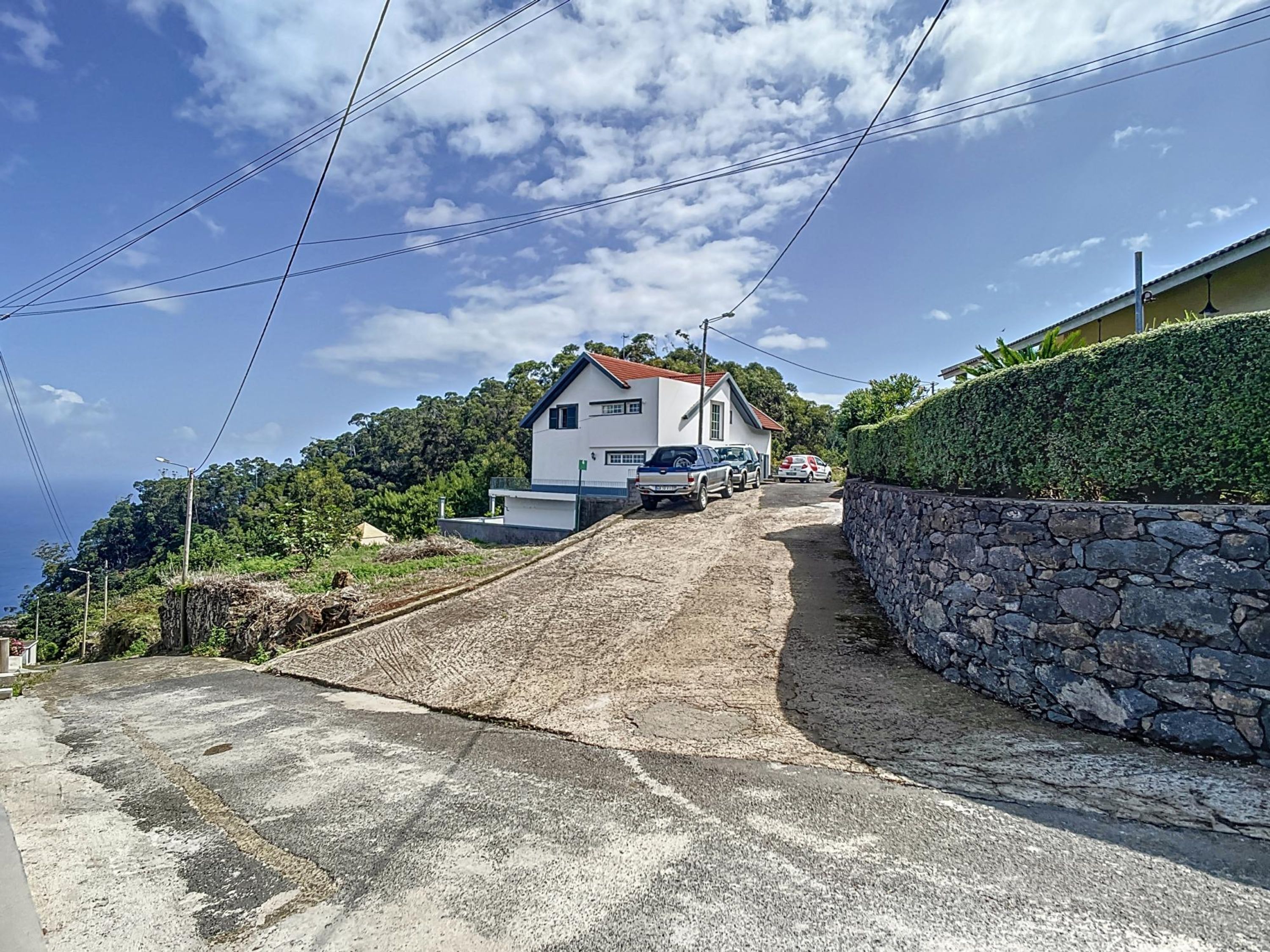 Une maison avec une allée en pente, un mur de pierre et une vue sur l’océan.