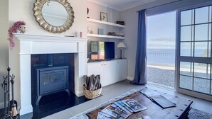 Una sala de estar con chimenea, televisor y vista al mar a través de un ventanal grande.