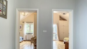 Un pasillo que conduce a dos habitaciones con piso de madera, un radiador, una silla y una cama con cabecera blanca.