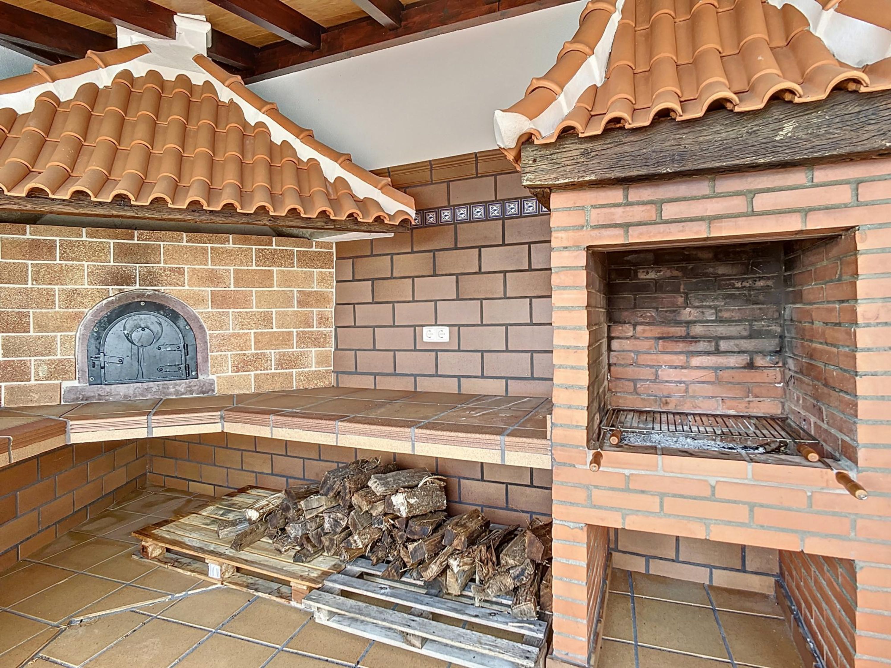A brick-built outdoor kitchen with a chimney, a fire pit, and a tiled floor.