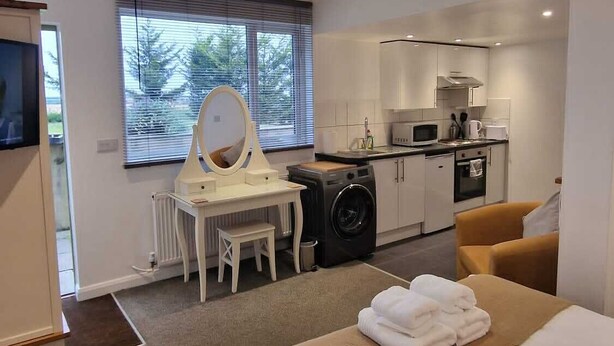 A modern hotel room with a large bed, a small kitchenette, a washing machine, and a bathroom with a mirror and toilet. - Charming Studio Rutland Point Holiday or Work (Oakham)