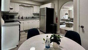 Une cuisine moderne avec des meubles blancs, un réfrigérateur en acier inoxydable et un coin repas comprenant une table et des chaises blanches.