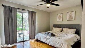 Une chambre avec un lit, un ventilateur de plafond et une vue sur l’extérieur, accessible par une porte-fenêtre coulissante.