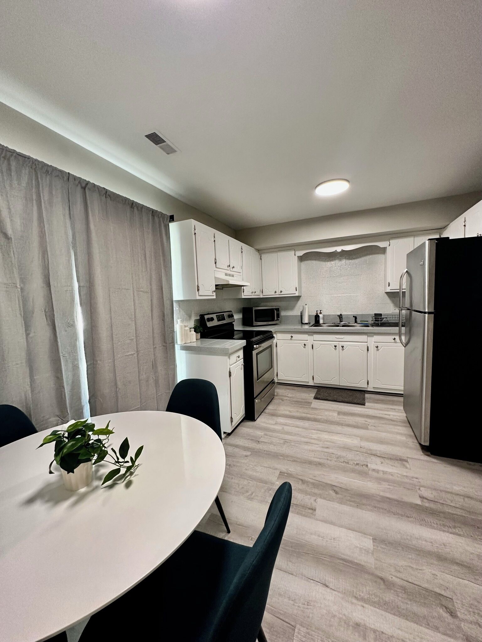 A modern kitchen with white cabinets, a black refrigerator, and a microwave.