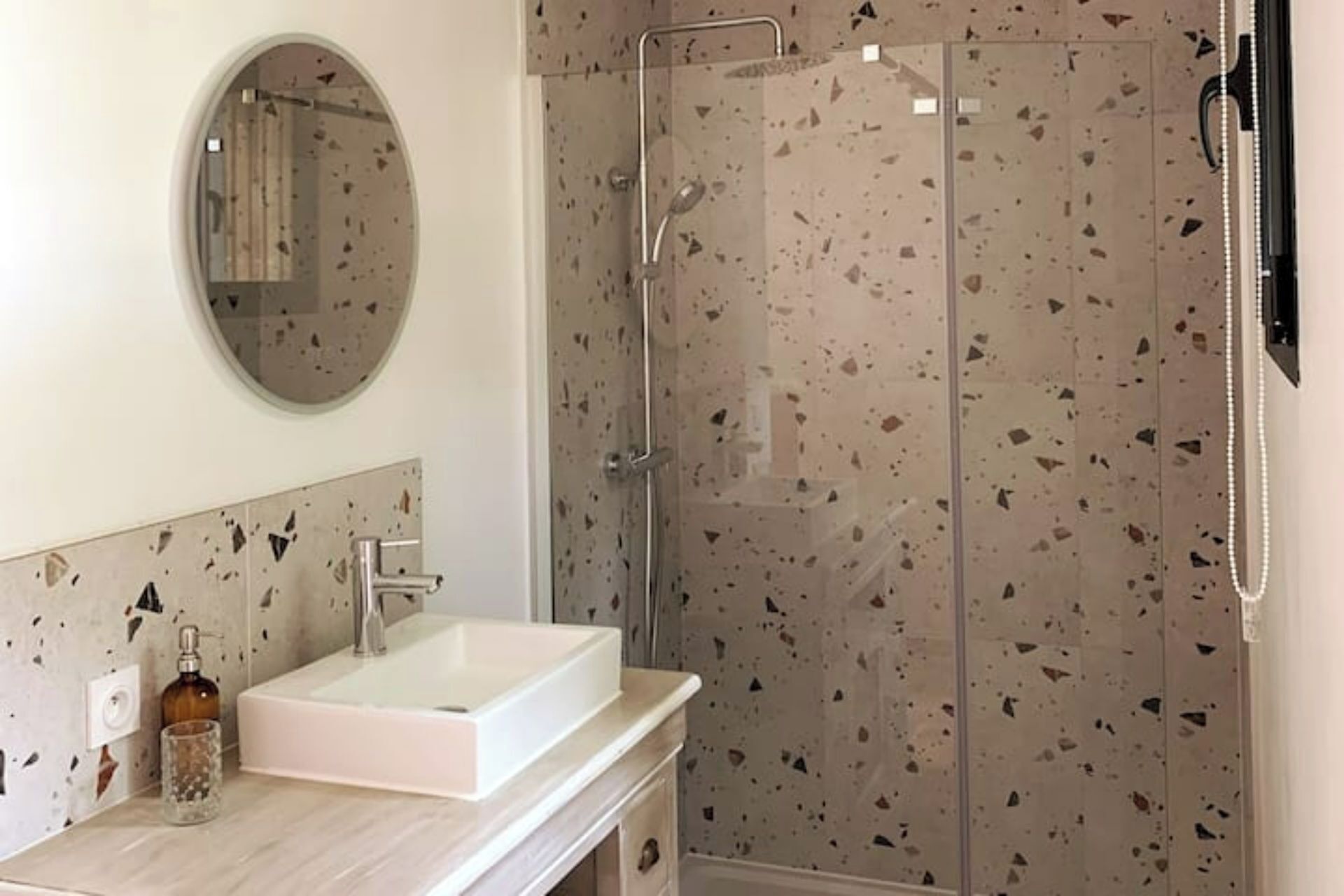 A bathroom with a white sink, a round mirror, and a shower with a glass door.