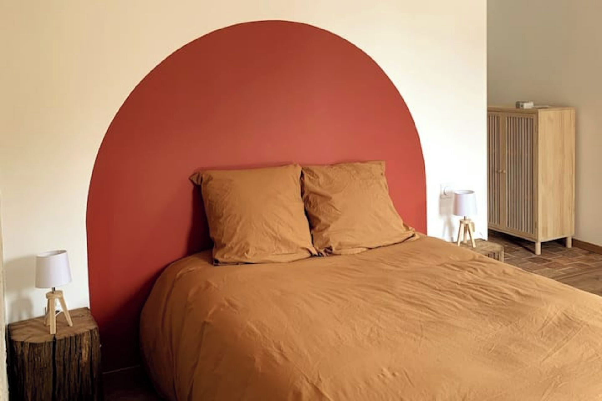 A bed with a large red arch headboard, two pillows, and a wooden side table with a lamp.