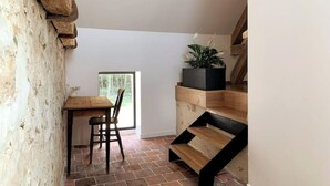 A rustic interior with a wooden table and chairs, a black planter with plants, and a brick floor. - Cottage au coeur du Perche (Souancé-au-Perche)