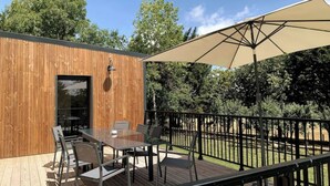 An outdoor deck with a wooden wall, a table with chairs, and a large umbrella. - Cottage au coeur du Perche (Souancé-au-Perche)