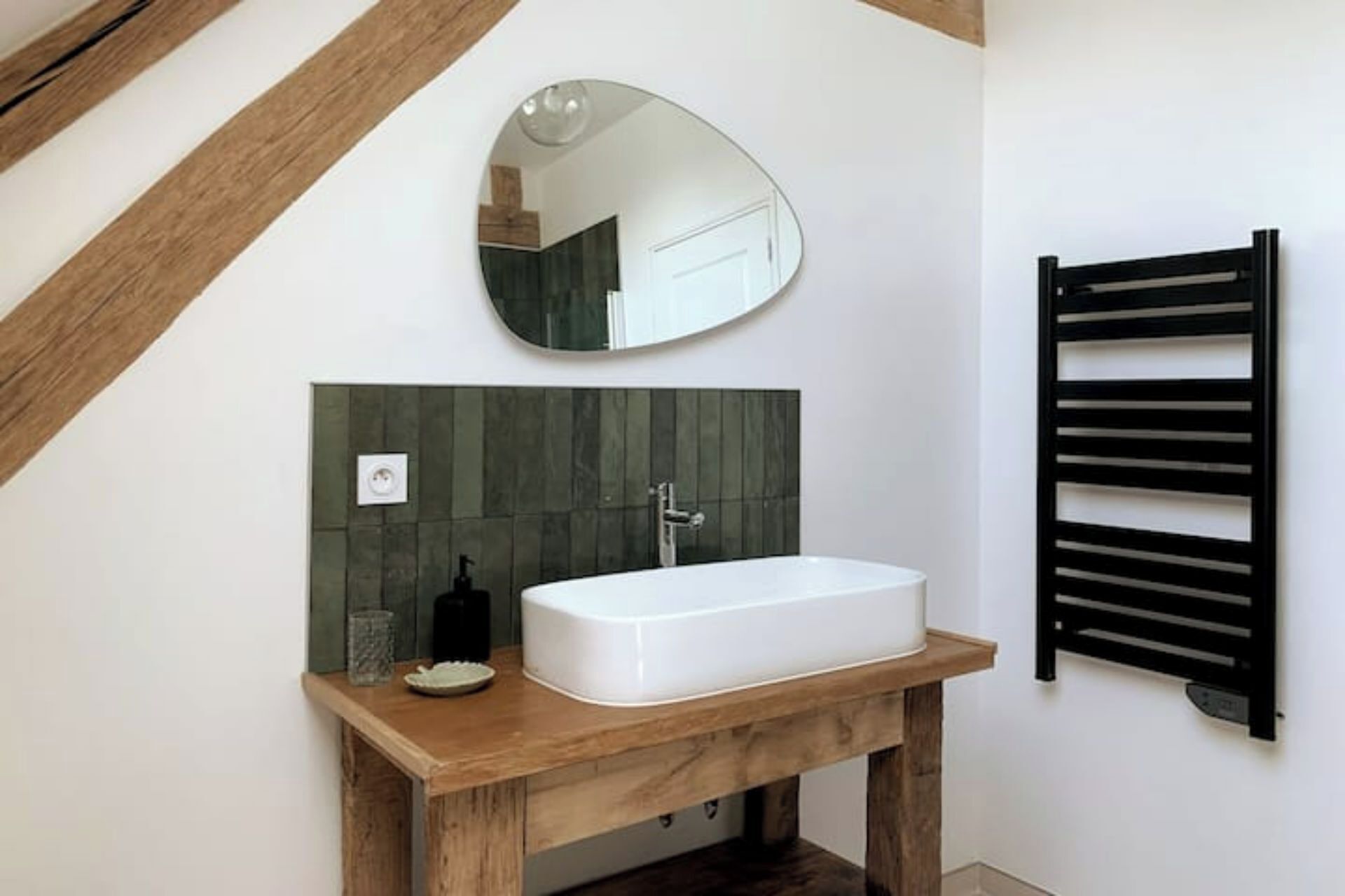 Un baño con tocador de madera, un lavamanos blanco, un espejo y un perchero negro.