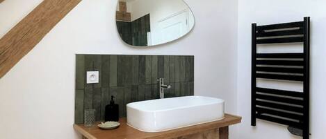 Un baño con tocador de madera, un lavamanos blanco, un espejo y un perchero negro.