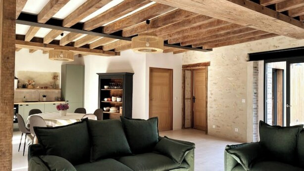 A modern interior with exposed wooden beams, a green sofa, a dining area, and a kitchen. - Cottage au coeur du Perche (Souancé-au-Perche)