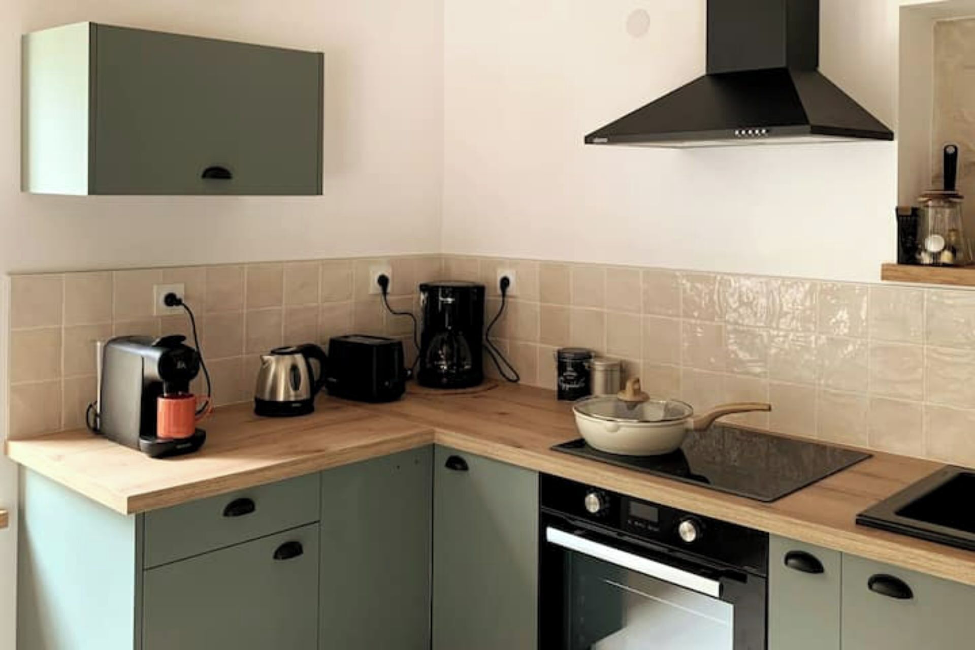 A kitchen with a built-in oven, a coffee maker, a kettle, and a toaster on the counter.