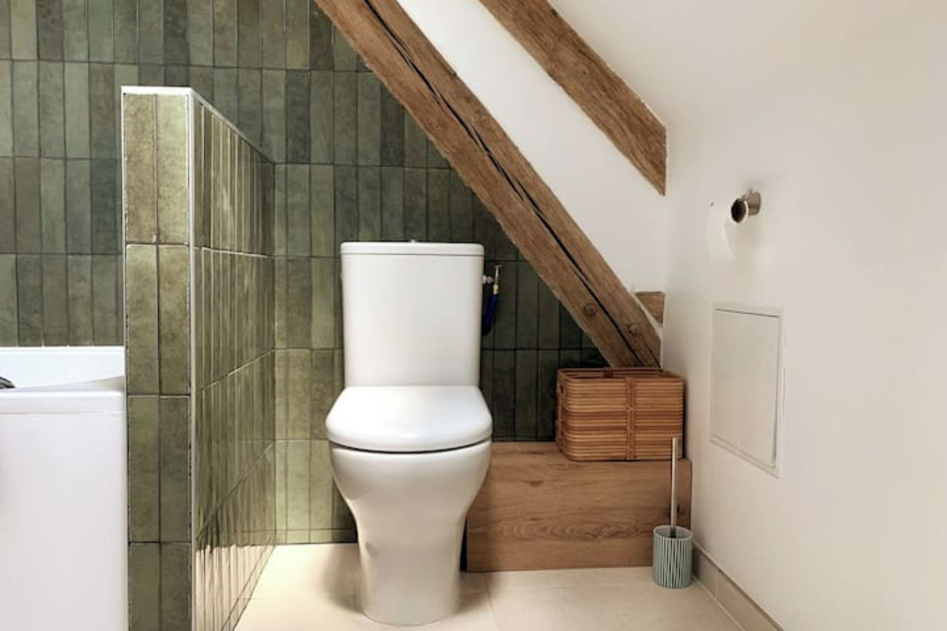 Une salle de bain moderne avec des toilettes blanches, des murs recouverts de carreaux verts, un plancher en bois et une petite boîte en bois.