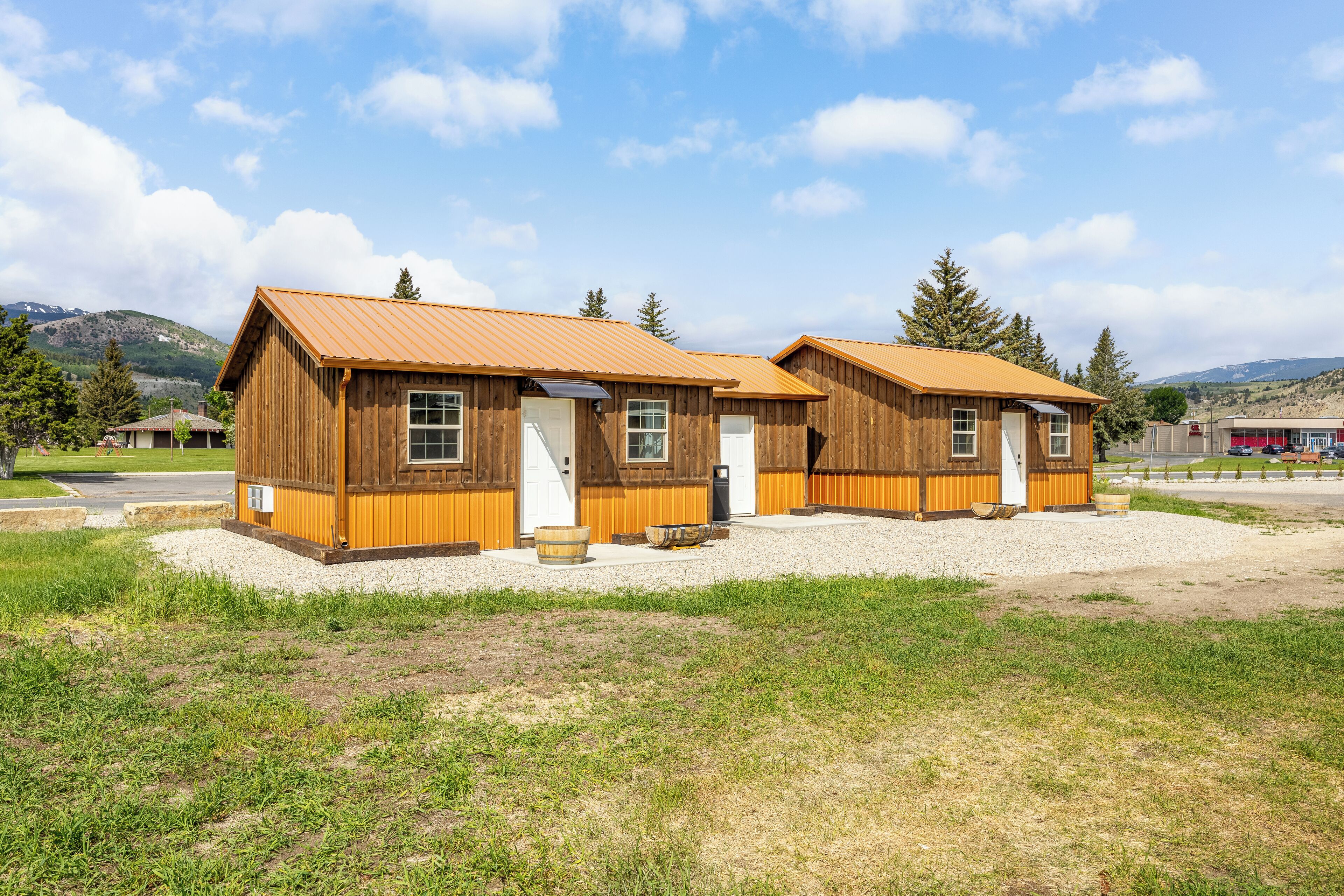 Two wooden cabins with metal roofs, a gravel driveway, and a grassy area.
