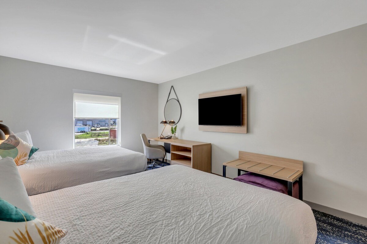 Habitación de hotel con dos camas, un escritorio, una silla, un televisor y una ventana con vistas.