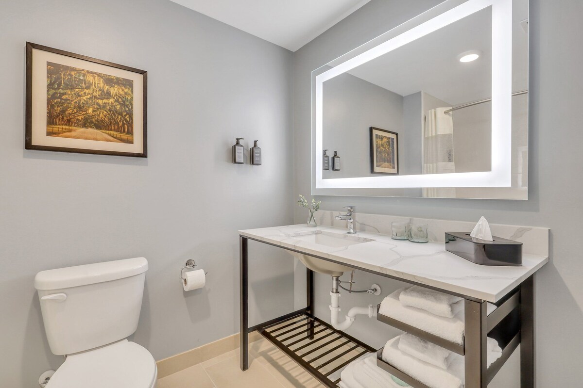 A modern bathroom with a white toilet, a large mirror, and a white sink.