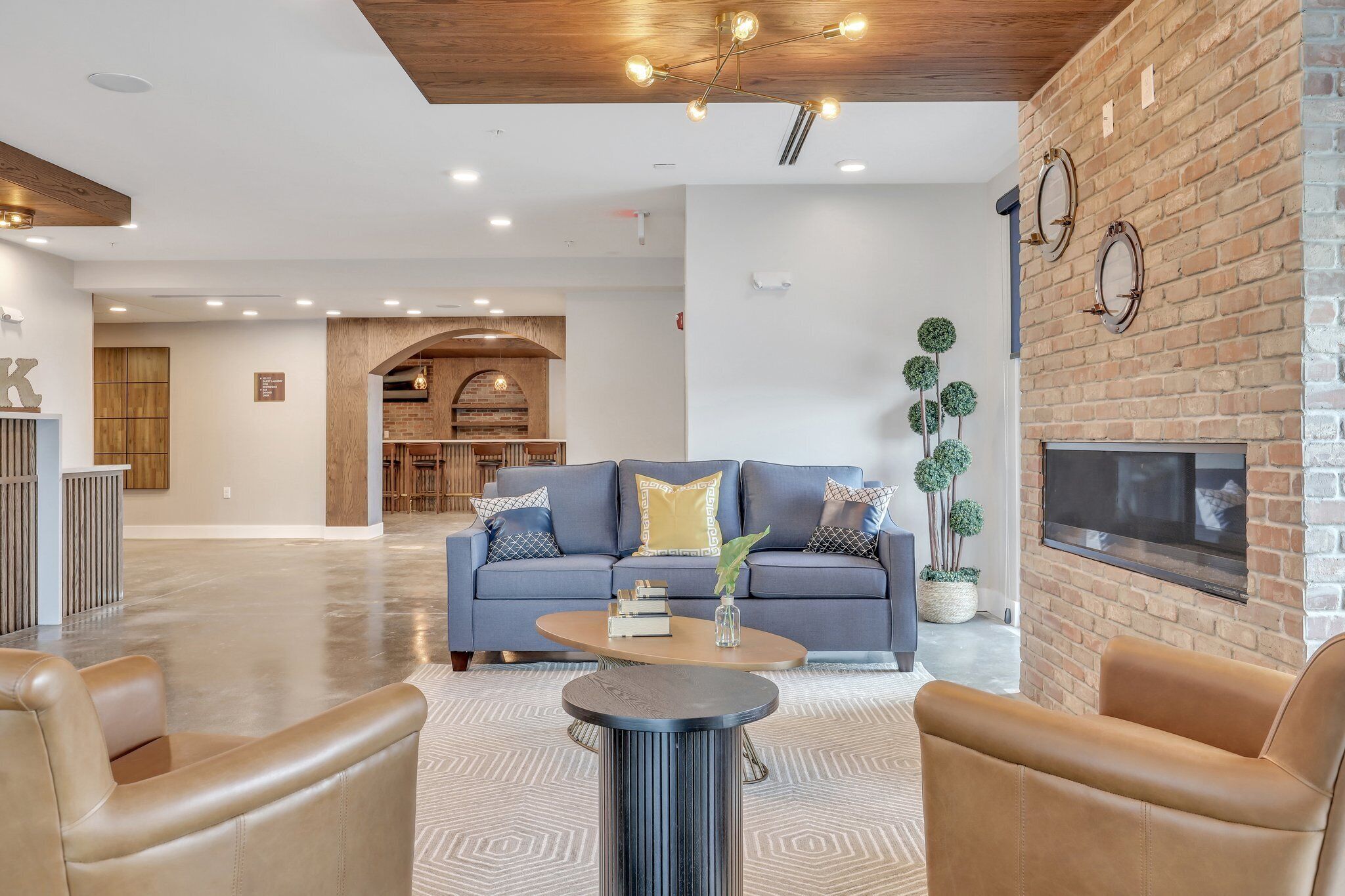 A modern living room with a blue sofa, leather armchairs, a coffee table, and a brick fireplace.