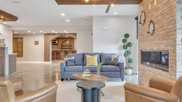 A modern living room with a blue sofa, leather armchairs, a coffee table, and a brick fireplace.