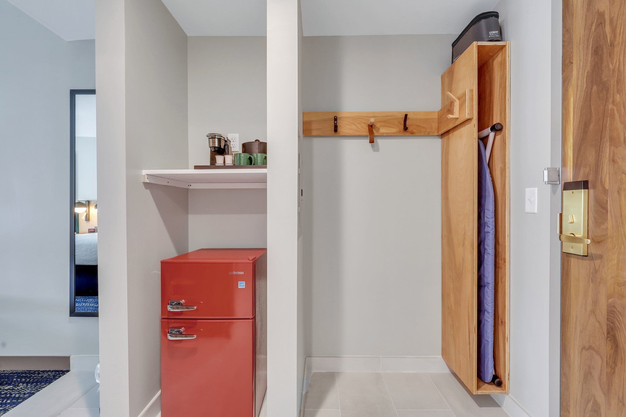 Una habitación compacta con un mueble de almacenamiento rojo, un armario de madera con perchero y una pequeña estantería con utensilios de cocina.