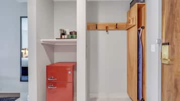 Una habitación compacta con un mueble de almacenamiento rojo, un armario de madera con perchero y una pequeña estantería con utensilios de cocina.