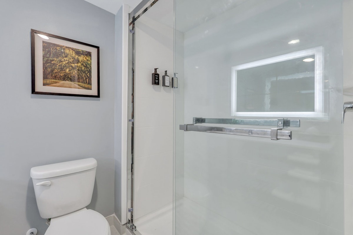 Un baño con cabina de ducha de vidrio, un cuadro en la pared y un inodoro.