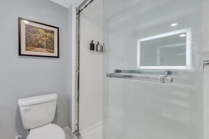 Uma casa de banho com cabine de duche em vidro, um quadro na parede e uma sanita.