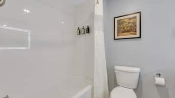 A bathroom with a bathtub, toilet, and a shower curtain. There are three bottles of toiletries on the wall.