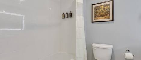 A bathroom with a bathtub, toilet, and a shower curtain. There are three bottles of toiletries on the wall.