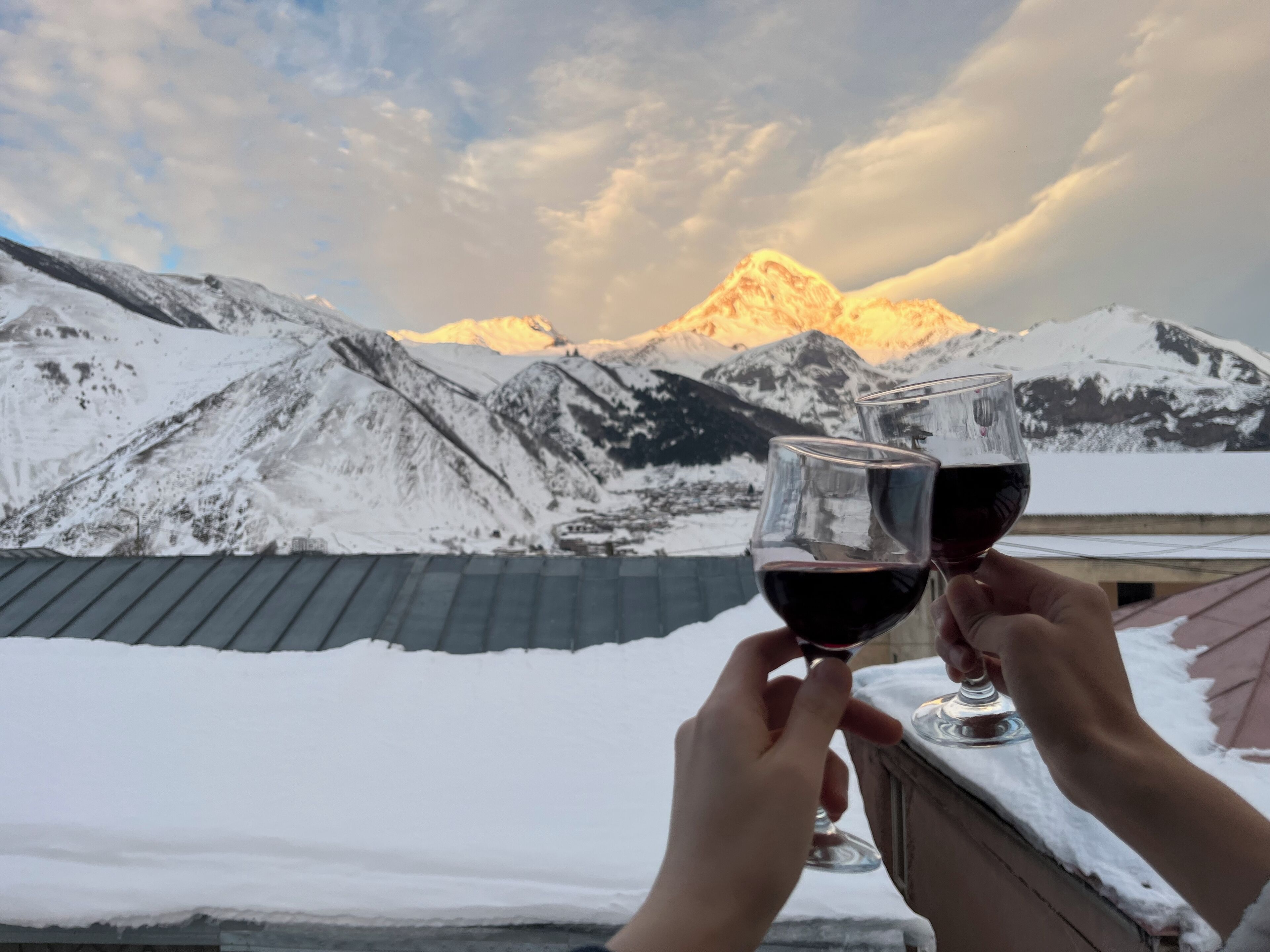Deux personnes tenant des verres à vin, avec un paysage de montagne enneigé en arrière-plan.